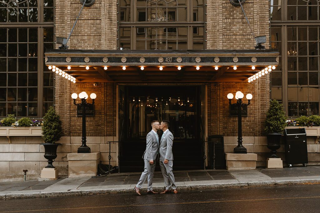 Two grooms kissing in front of a vintage hotel