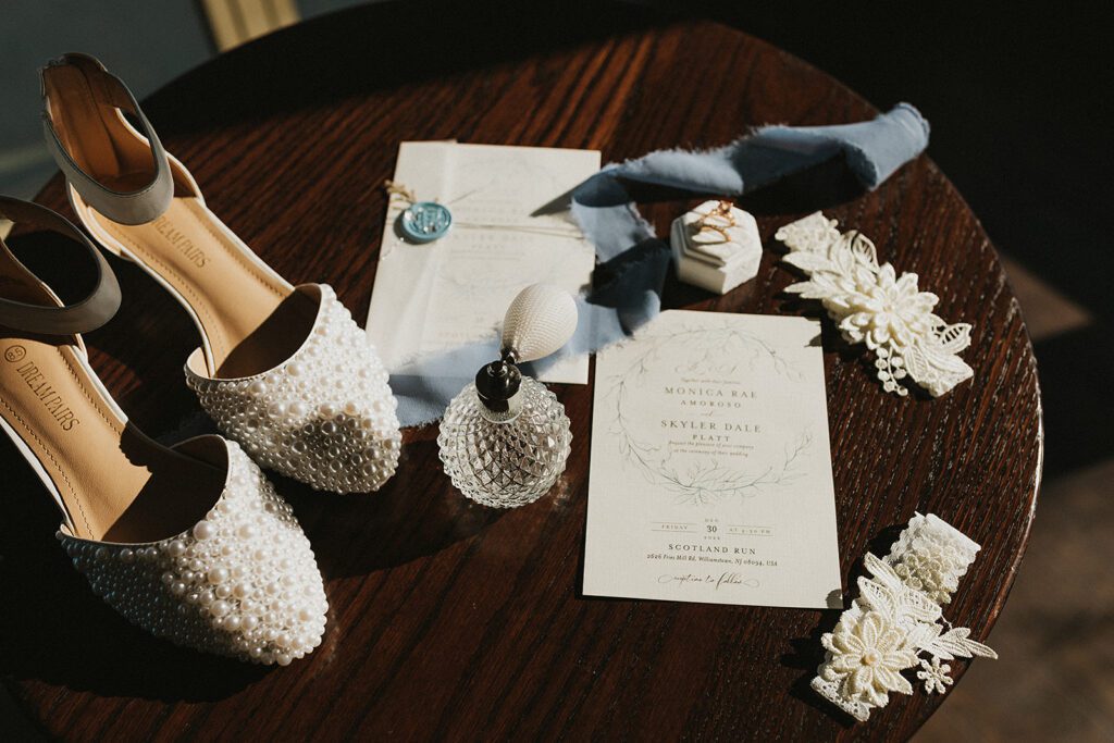 A beautiful wedding detail shot of pearl wedding shoes, lace, perfume, invitations and wedding rings