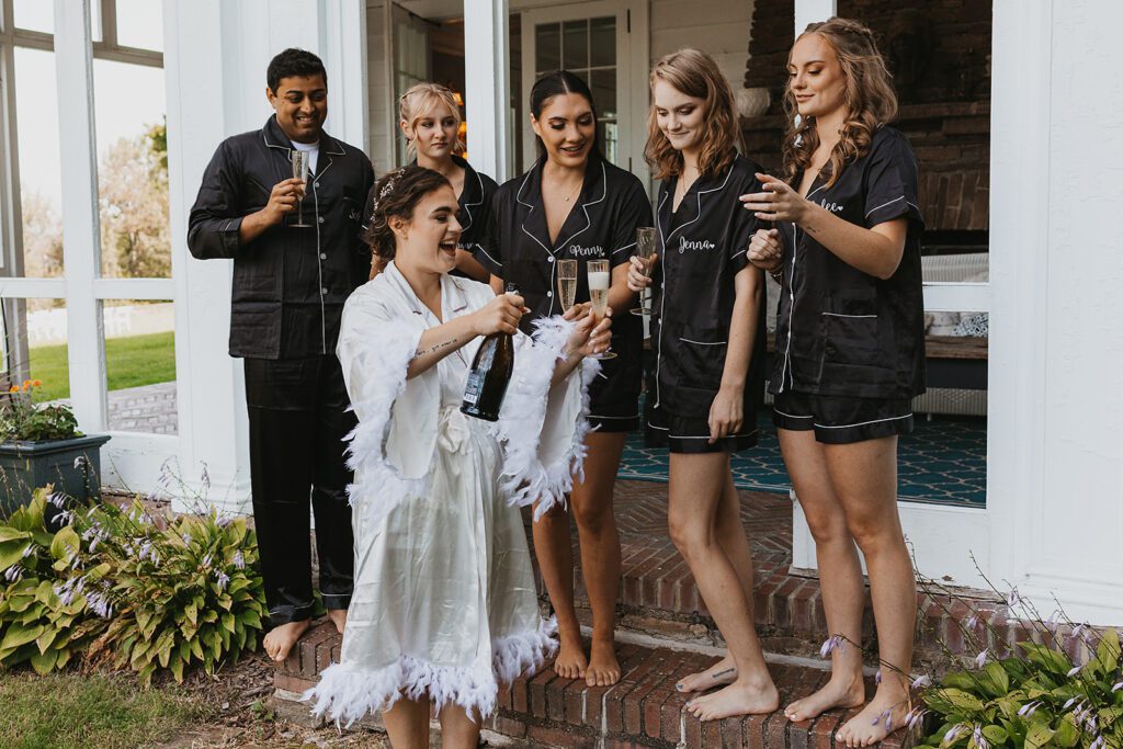 bride popping champagne with her bridal party in the backdrop in black silk PJs