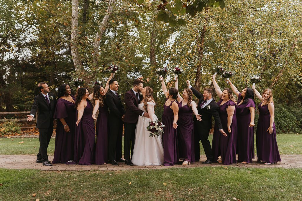 Lively group photo of bridesmaids in elegant purple dresses and groomsmen in purple ties, celebrating a Jewish wedding at a country club
