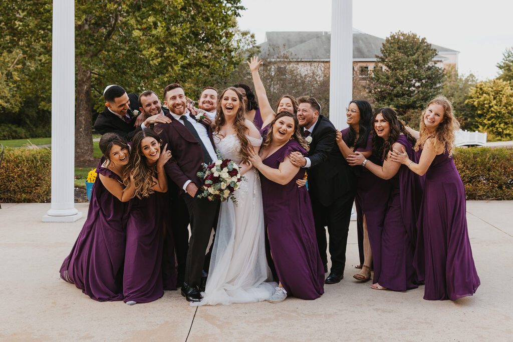 Bridal party posing playfully, bridesmaids in purple dresses and groomsmen with matching purple ties, at a Jewish country club wedding