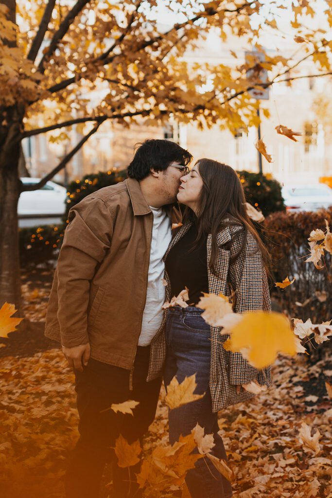 Candid laughter and joy radiate from Alexa and Joe as they indulge in a playful leaf fight, a moment of pure bliss during their fall engagement photo shoot in Palmer Square
