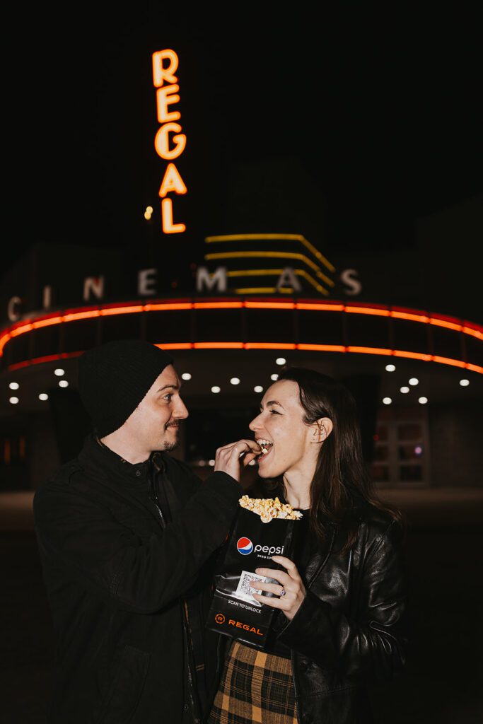 Engaged couple, Christine and Joe, striking a casual pose with the charming facade of a movie theater in the background, perfect for their movie theater-themed engagement photos