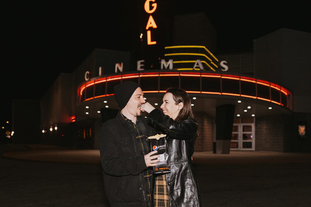 Christine and Joe sharing a tender moment in front of a quaint movie theater, the marquee lights adding a magical touch to their movie theater engagement photos.