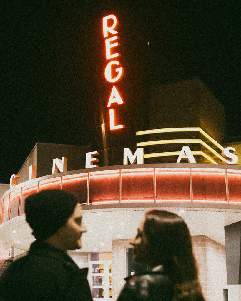 Christine and Joe sharing a tender moment in front of a quaint movie theater, the marquee lights adding a magical touch to their movie theater engagement photos