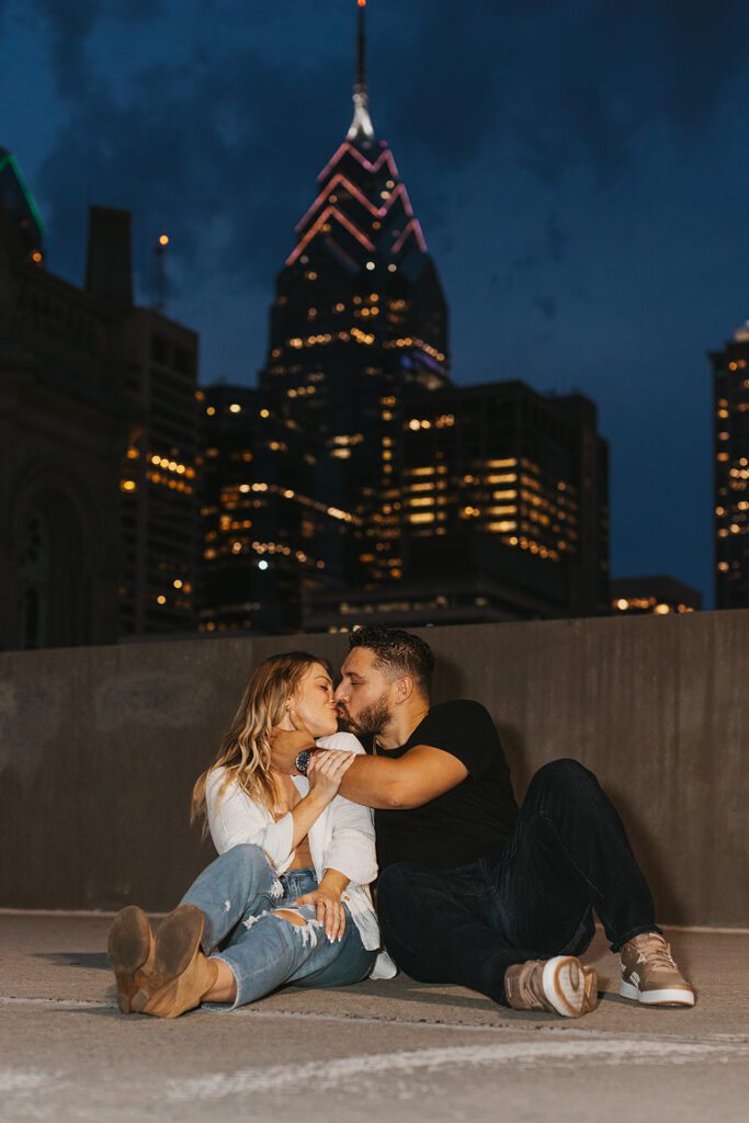 engaged couple on a rooftop with nighttime city skyline in the backdrop