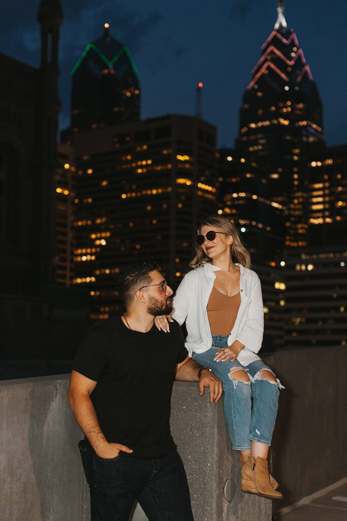 engaged couple on a rooftop with nighttime city skyline in the backdrop