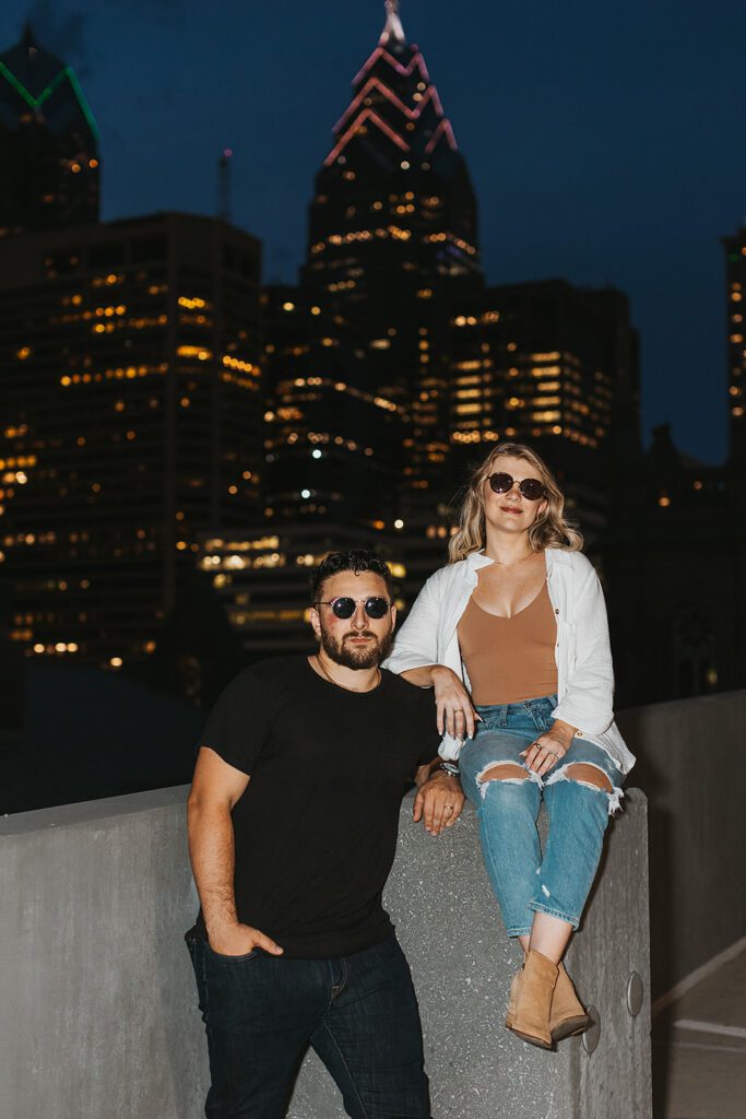 engaged couple on a rooftop with nighttime city skyline in the backdrop