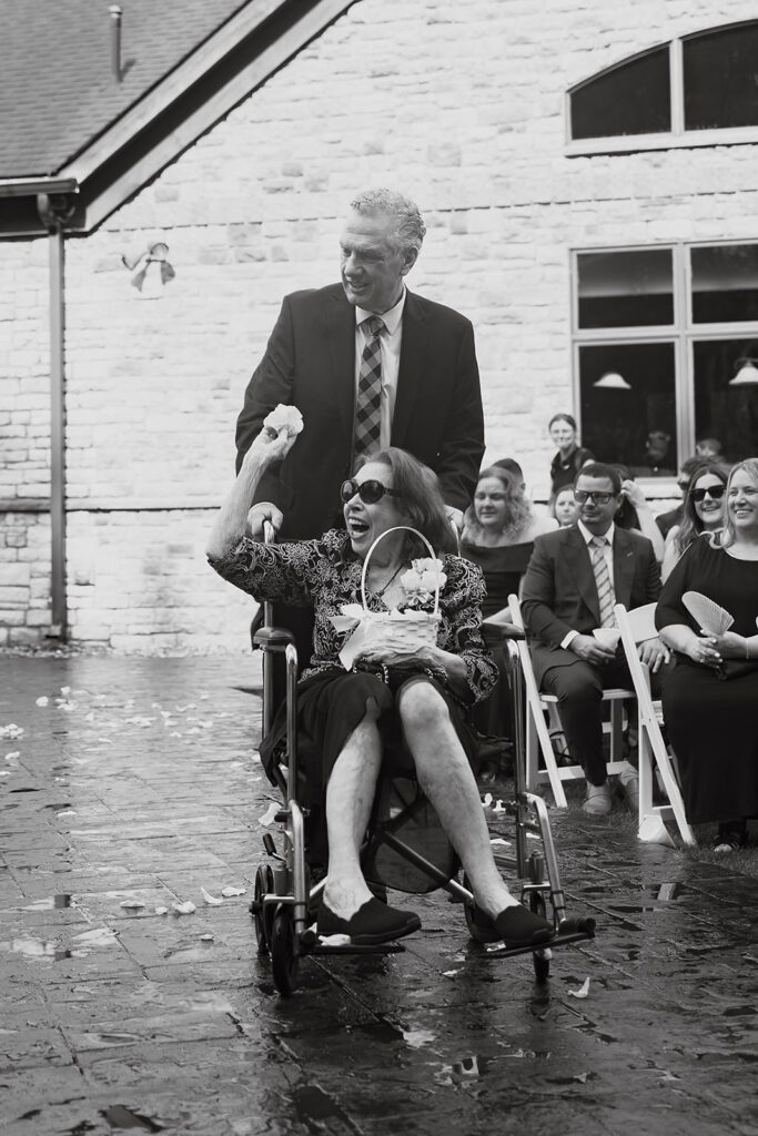 Grandma as a flower girl is going down the aisle in a wheelchair sprinkling petals on the aisle