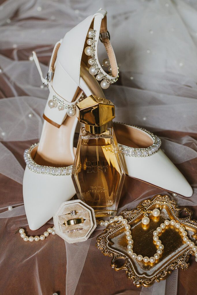 A close-up shot of the bride's pearl-embellished wedding shoes, accompanied by a velvet ring box displaying both the wedding bands and the engagement ring