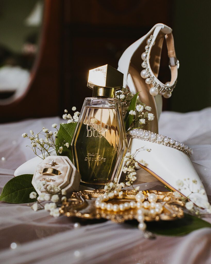 A close-up shot of the bride's pearl-embellished wedding shoes, accompanied by a velvet ring box displaying both the wedding bands and the engagement ring