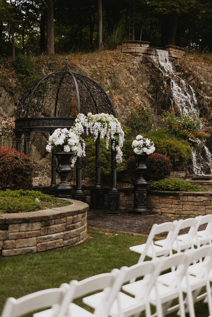 A beautifully ornate black metal gazebo is adorned with cascading white floral arrangements for a Stroudsmoor Country Inn wedding ceremony