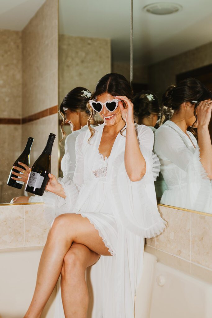 bride sitting in the tub in a cute nightgown with a bottle of champagne