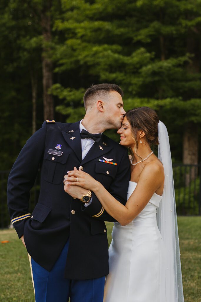 The groom, in a formal military uniform, is kissing the beautiful bride on the forehead