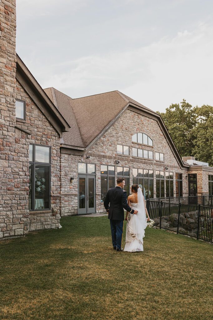 The bride and groom share a quiet moment walking hand-in-hand in front of a beautiful stone mansion - the Stroudsmoor Country Inn