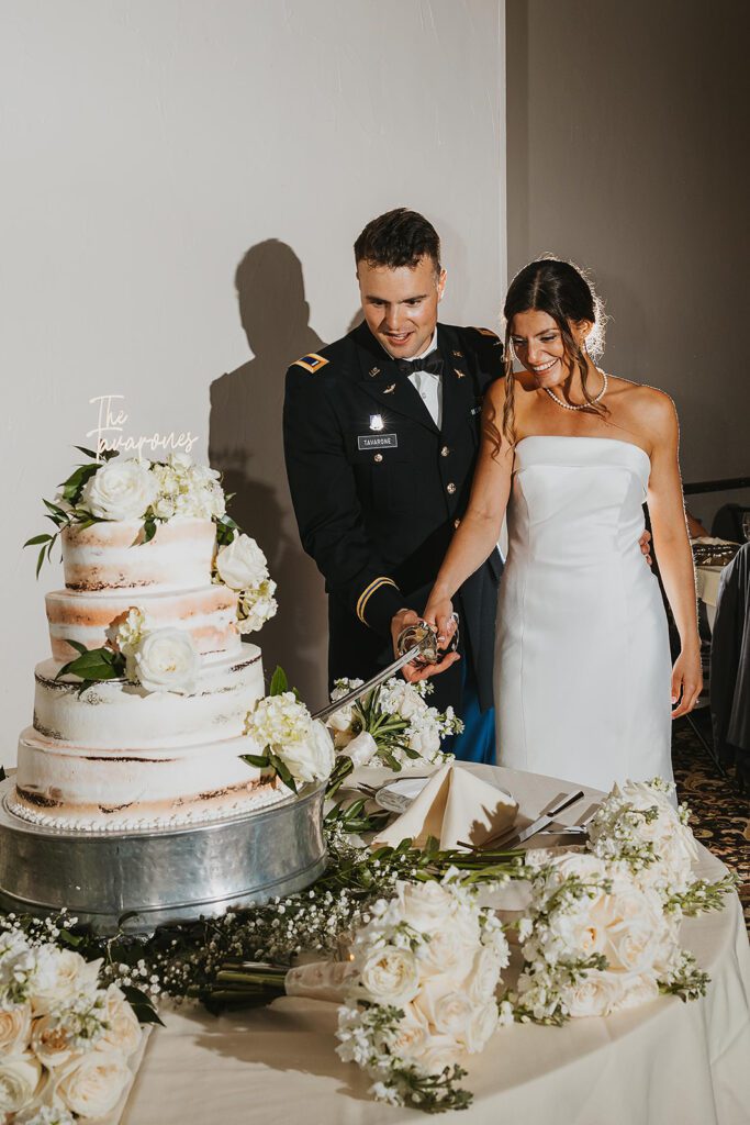 The bride and groom cut their multi-tiered wedding cake together using a ceremonial sword